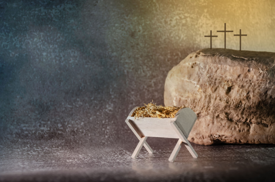 Eine Miniatur-Krippe vor einem Fels auf dem 3 Kreuze stehen.