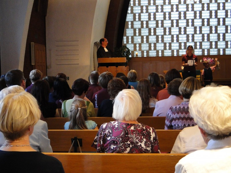 Menschen auf Kirchenbänken sitzend dem Pfarrer bei der Predigt lauschen