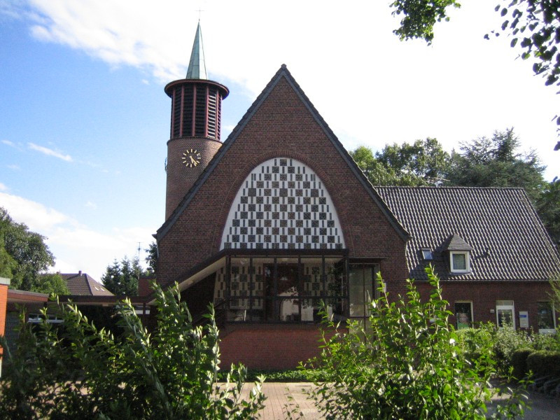 Frontalansicht Kirchenschiff und Turm, davor grüne Büsche