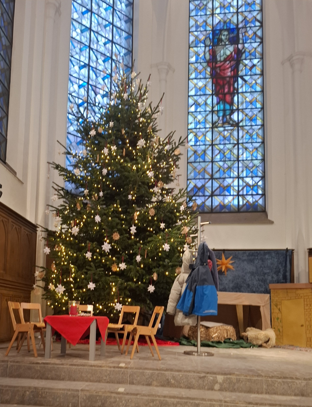 Geschmückter Weihnachtsbaum im Altarraum der Stadtkirche Moers. Davor ein Tisch und 5 leere Stühle.
