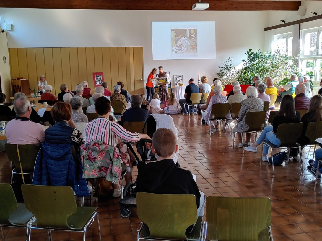 Gottesdienstbesucher im großen Saal sitzend lauschen dem Schauspiel vorne.