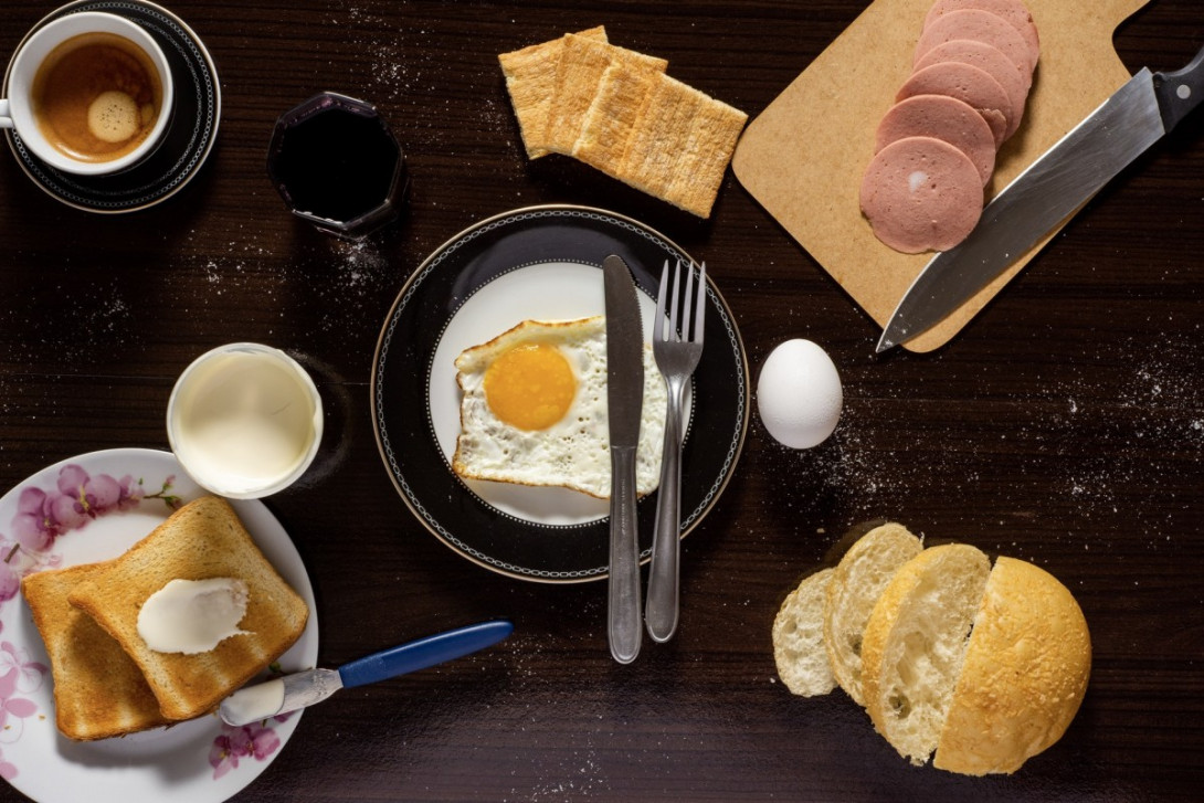 Ein Frühstückstisch von oben: Toast, Rührei, Brötchen, Wurst, Kaffee, Milch