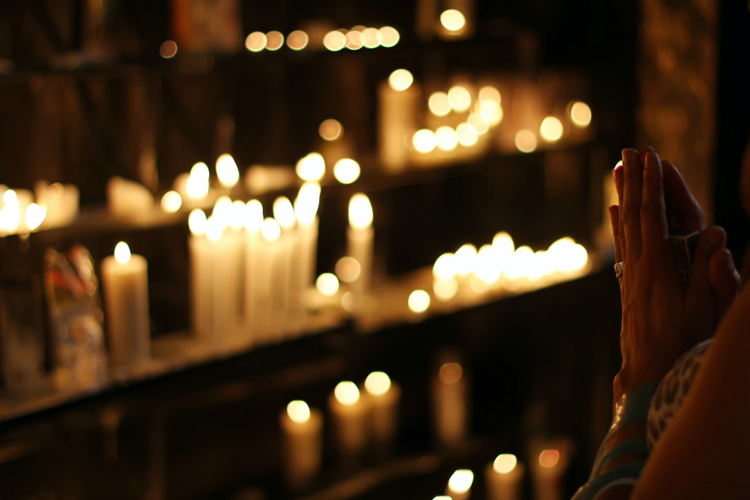 betende Hände vor einem mehrstöckigem Kerzenständer in einer Kirche