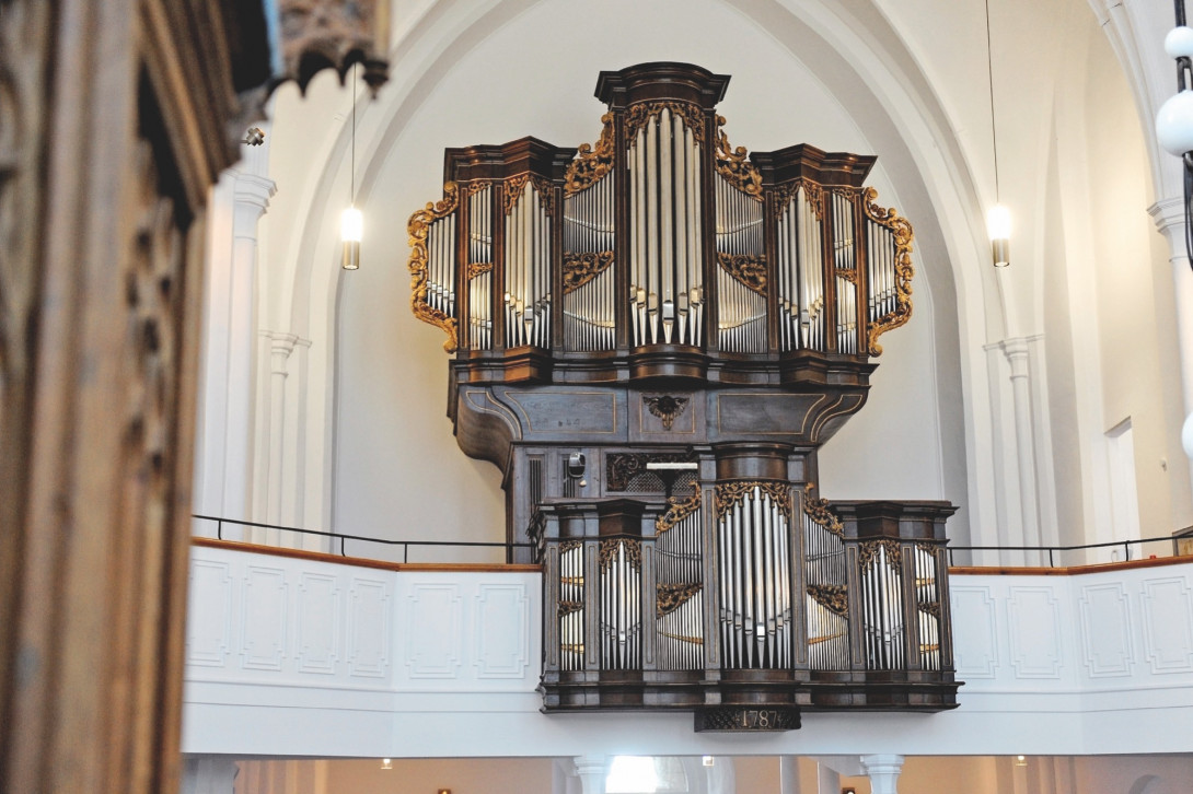 Die imposante Orgel in der Stadtkirche Moers. Eine dunkle Orgel mit glänzenden Pfeifen vor weißer Wand.